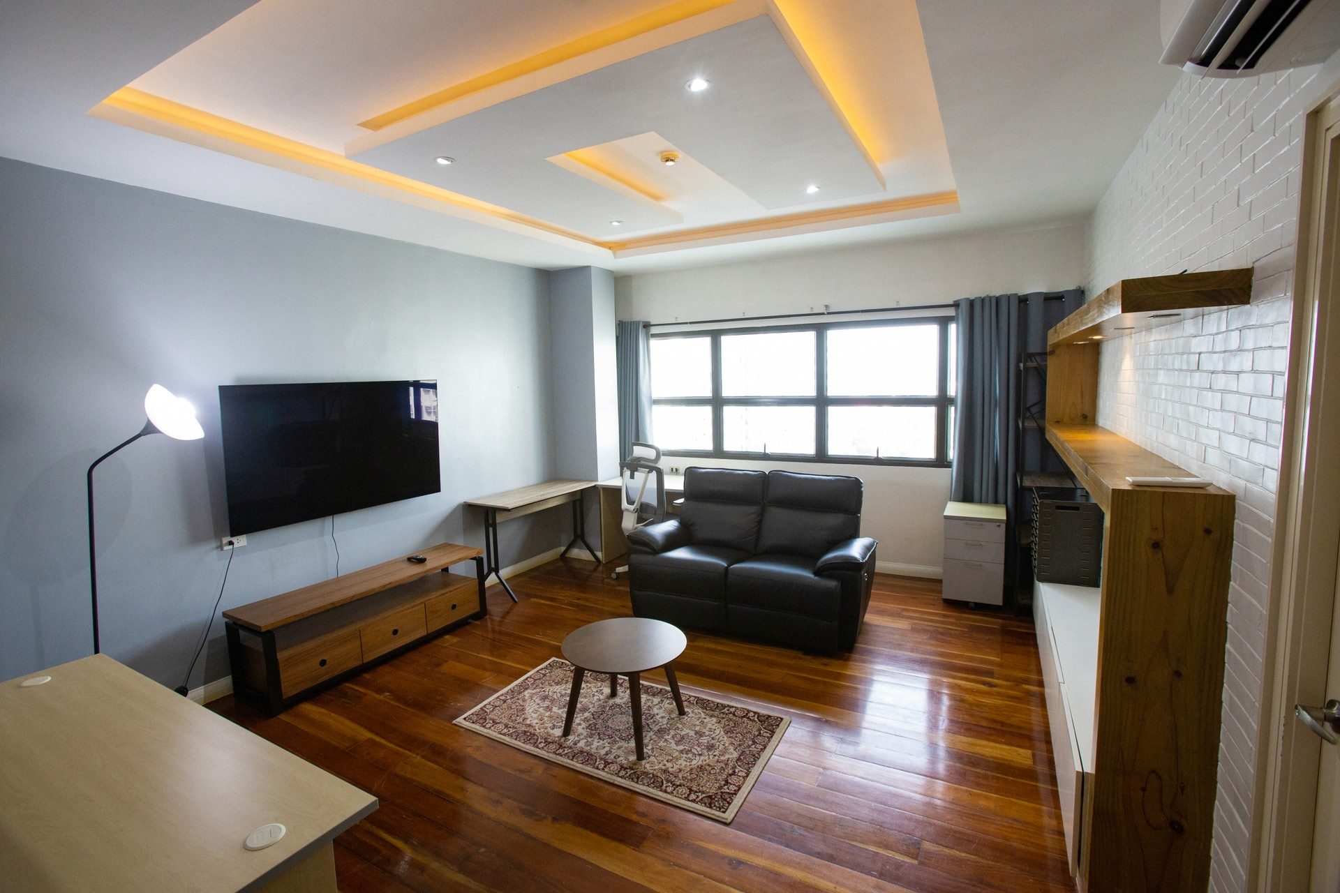 Apartment 1809 living room with wood-toned flooring, a black sofa and warm recessed ceiling lighting