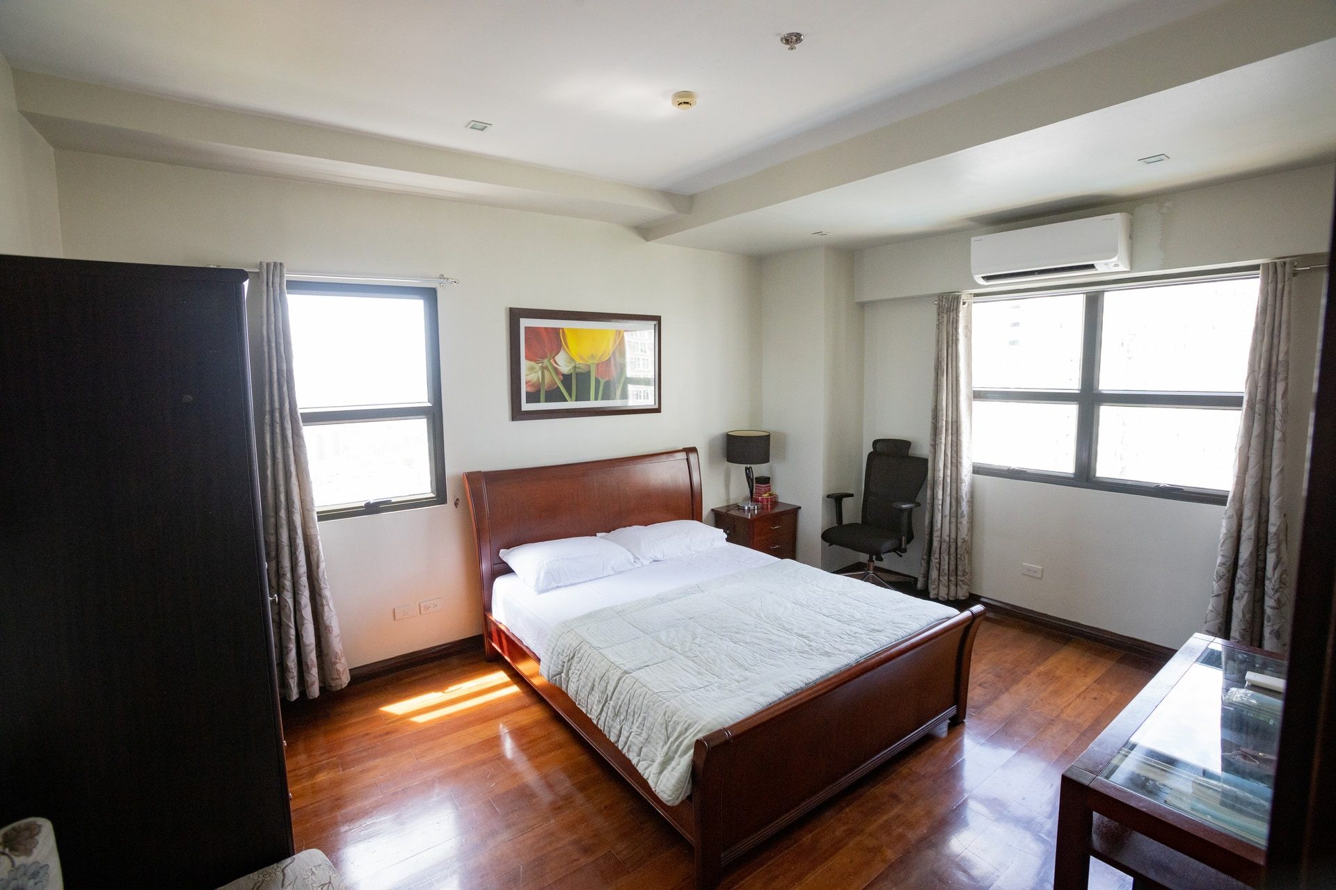 Apartment 1810 bedroom with a wooden double bed, wood-toned flooring and light curtains