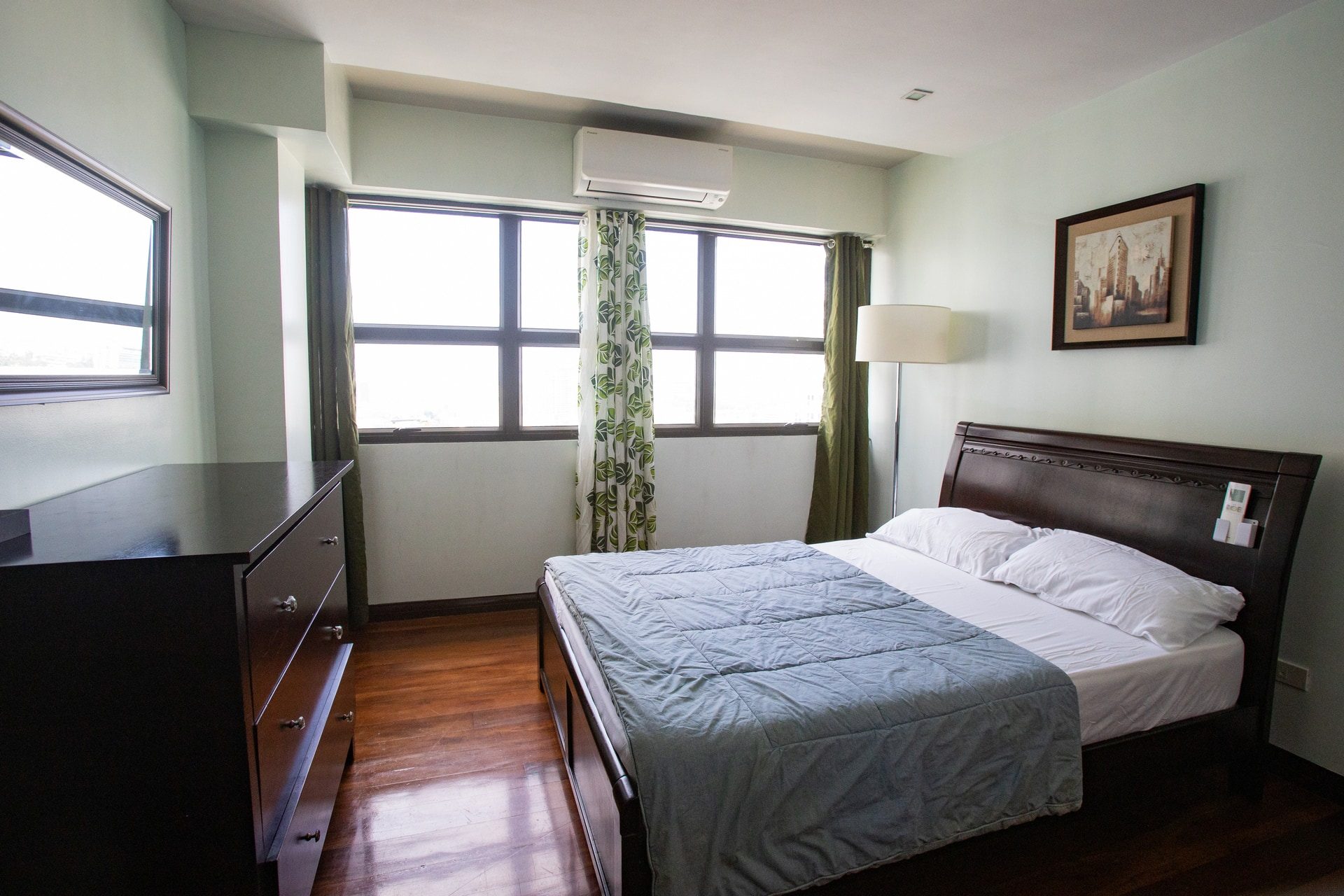 Apartment 1810 bedroom with a double bed, green curtains and windows on two walls