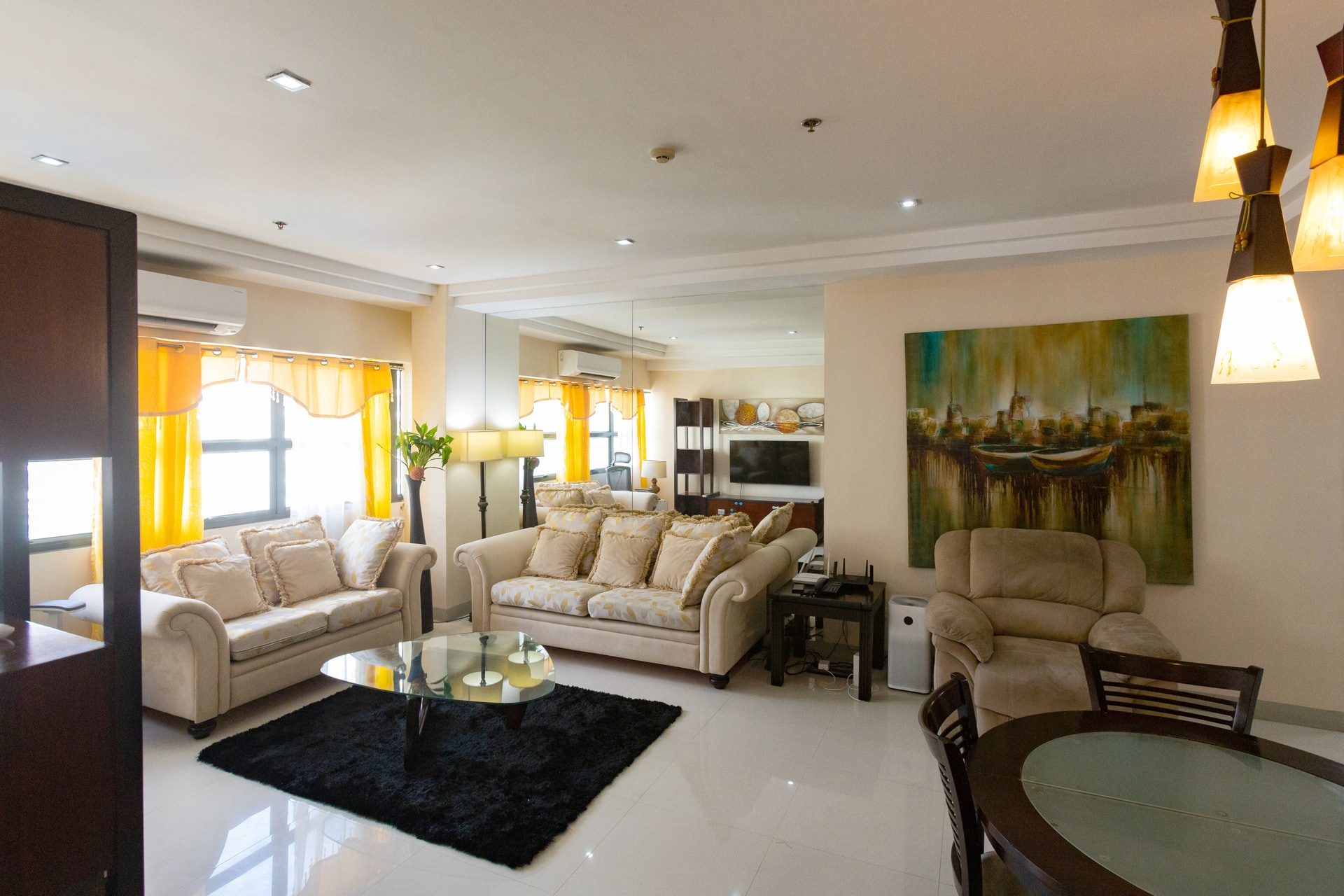 Apartment 1810 living and dining area with cream sofas, yellow curtains and a glass-topped dining table