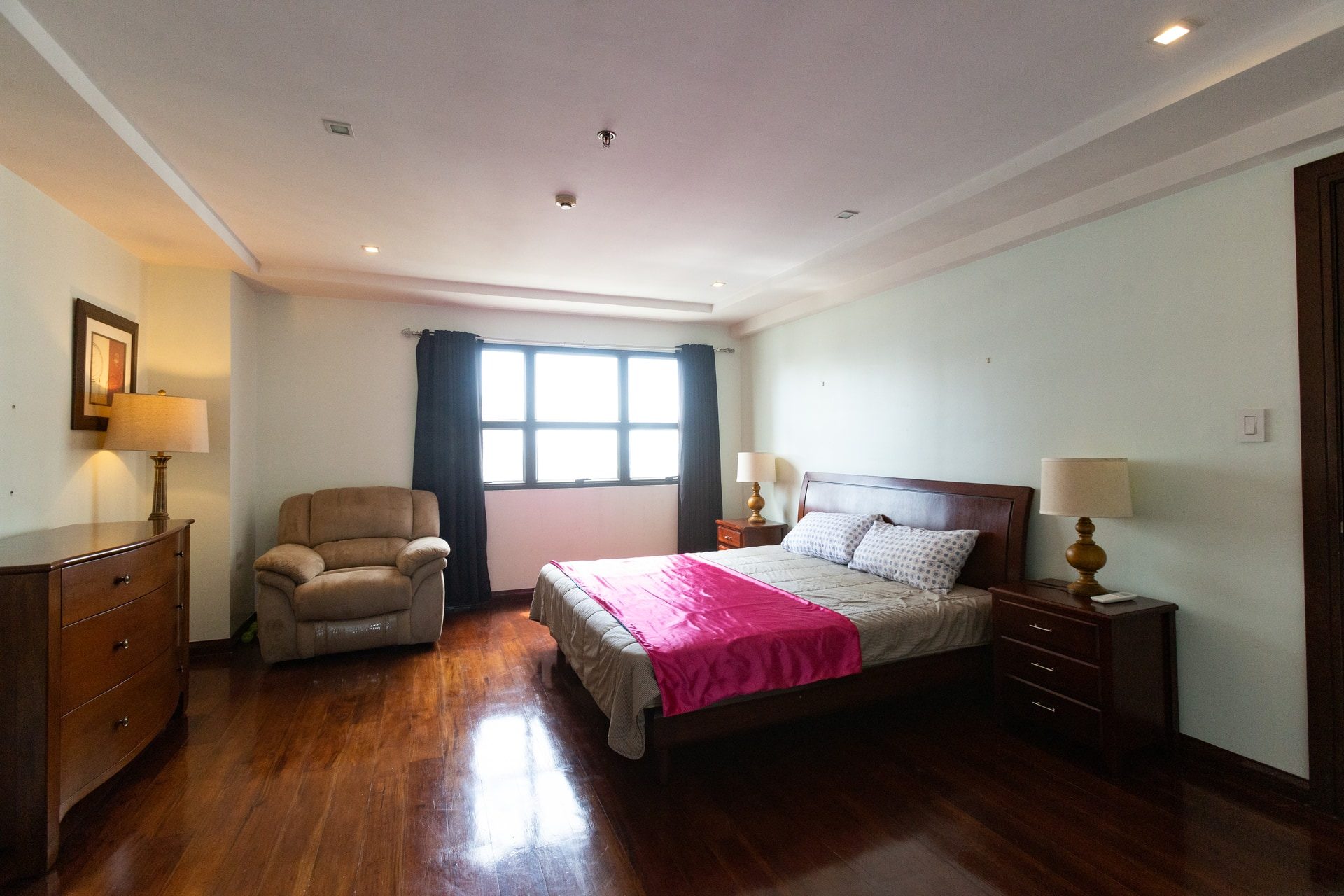 Apartment 1810 main bedroom with wood-toned flooring, a double bed and a reading chair